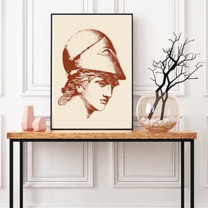 May include: A framed print of a line drawing of a woman wearing a helmet with an all-seeing eye design. The drawing is in shades of brown on a cream background.
