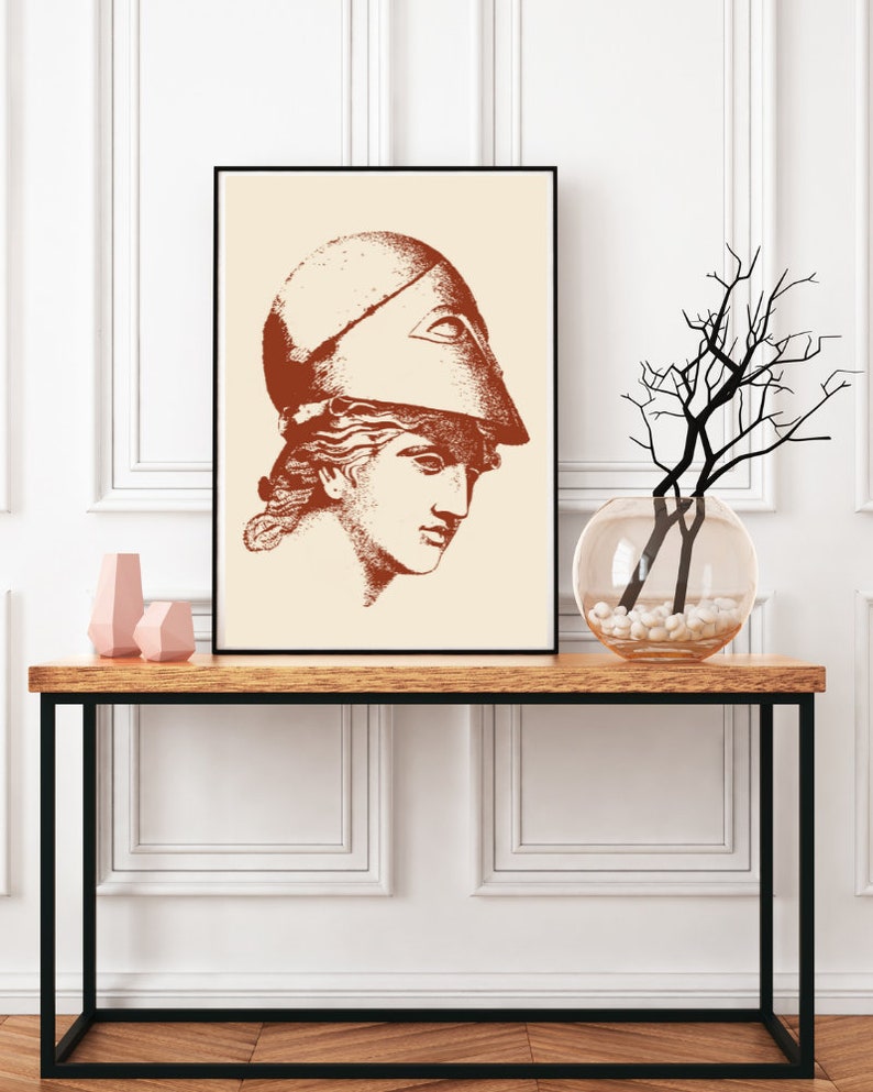 May include: A framed print of a line drawing of a woman wearing a helmet with an all-seeing eye design. The drawing is in shades of brown on a cream background.