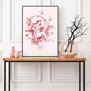May include: A framed print of a red illustration of a woman sitting on a brick wall with a lyre and birds. The text "Sappho" is below the image.