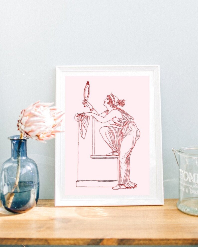 May include: A framed print of a line drawing of a woman in a long dress holding a mirror. The woman is standing on a platform and the drawing is in red on a pink background.