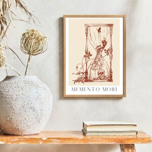 May include: A framed print featuring a red hourglass illustration with the text "MEMENTO MORI". The hourglass is surrounded by vines and a skull.