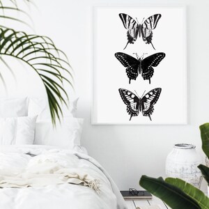 May include: A black and white framed print of three butterflies. The butterflies are arranged vertically, with the largest butterfly at the bottom and the smallest butterfly at the top. The butterflies are all in flight, with their wings spread out.