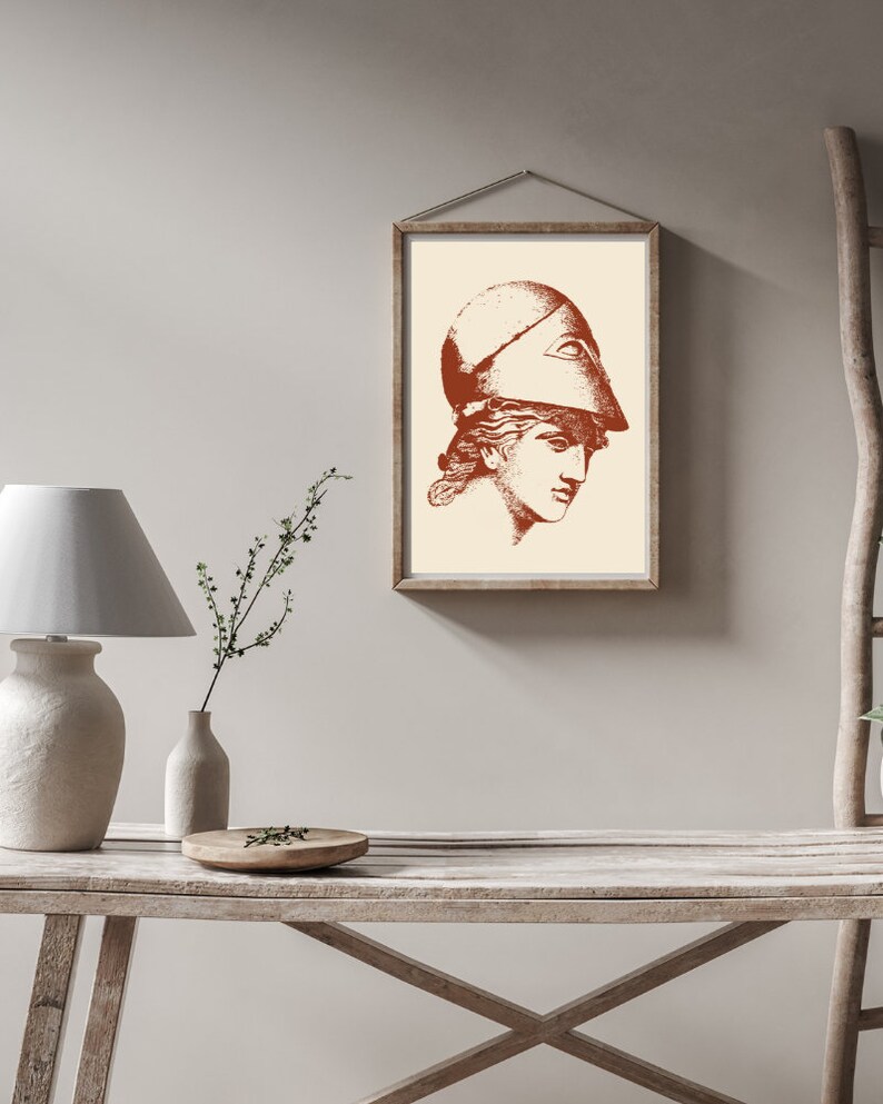 May include: A framed print of a woman's head wearing a helmet. The print is in shades of brown and white and is set against a light beige wall.