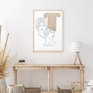 May include: A line art print of two classical busts with a brown column behind them. The print is framed in a light wood frame and is hanging on a white wall above a wooden console table.