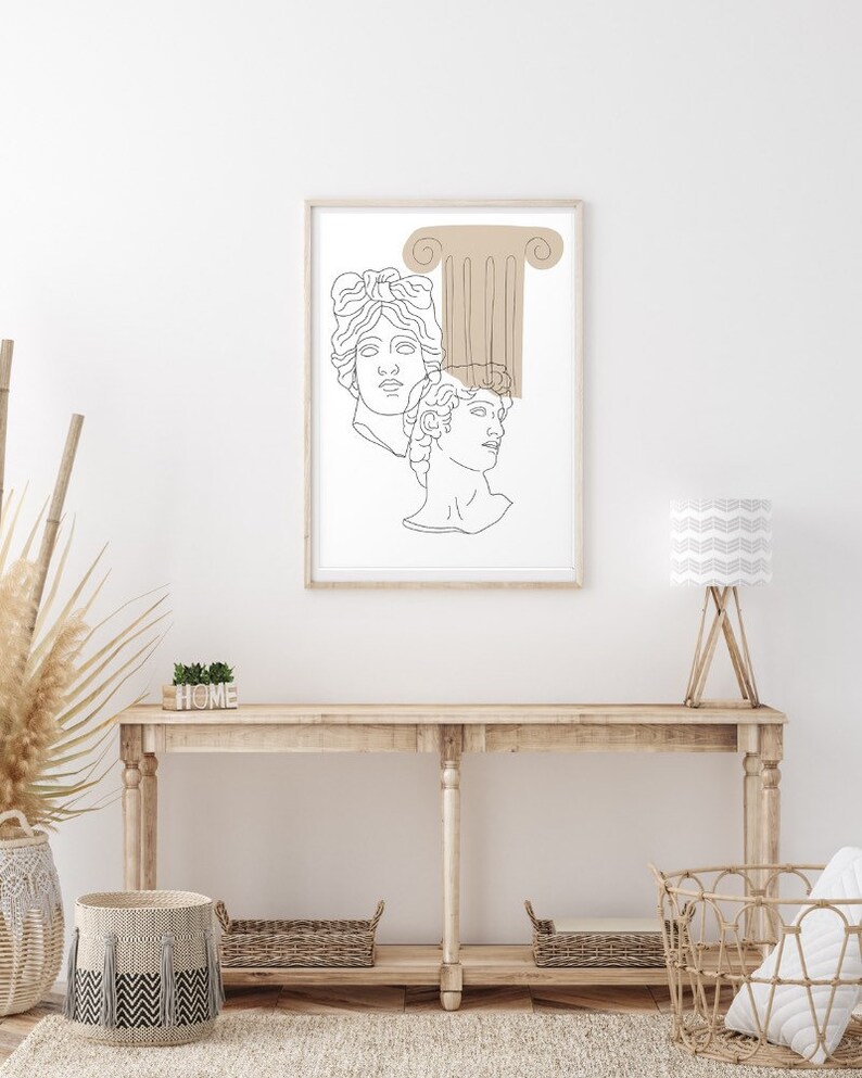 May include: A line art print of two classical busts with a brown column behind them. The print is framed in a light wood frame and is hanging on a white wall above a wooden console table.