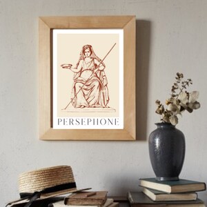 May include: A framed print of a line drawing of Persephone, a Greek goddess, in a seated pose. She is holding a bowl in her left hand and a staff in her right hand. The print is on a cream background with the word "PERSEPHONE" printed in brown below the image.