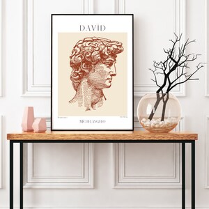 May include: A black framed print with a beige background featuring a line drawing of the David statue by Michelangelo. The title "DAVID" is printed in brown at the top of the print. The artist's name "MICHELANGELO" is printed in brown at the bottom of the print.
