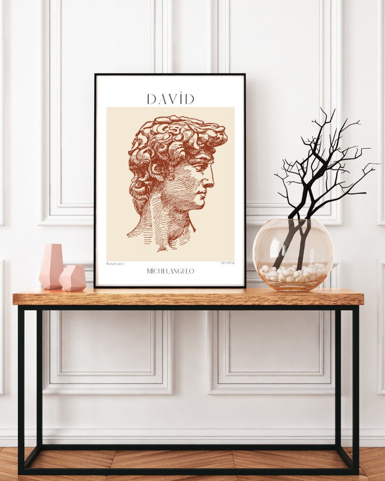 May include: A black framed print with a beige background featuring a line drawing of the David statue by Michelangelo. The title "DAVID" is printed in brown at the top of the print. The artist's name "MICHELANGELO" is printed in brown at the bottom of the print.