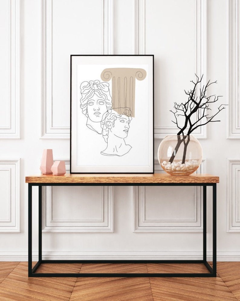 May include: A black framed print with a line drawing of two faces and a column in beige. The print is hanging on a white wall above a black metal console table with a wooden top. Two pink geometric vases are on the table.