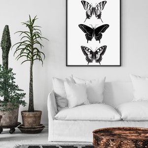 May include: Black and white framed print of three butterflies with a white background. The butterflies are arranged vertically, with the largest butterfly at the bottom and the smallest butterfly at the top.