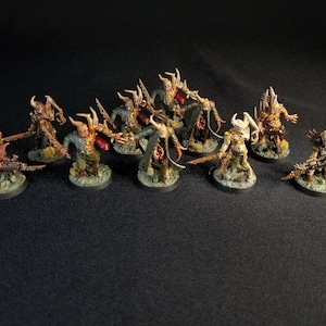 May include: A group of 12 painted miniature figures, depicting demonic creatures with horns, claws, and weapons. The figures are posed in a variety of fighting stances and are painted in shades of brown, green, and yellow.