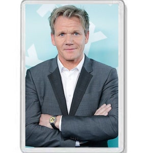 May include: A man with short, light brown hair is wearing a dark gray suit jacket with a white collared shirt underneath. He has his arms crossed and is wearing a silver watch with a yellow face.