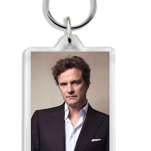 May include: A clear acrylic keychain with a photo of a man with brown hair wearing a black suit and white shirt.