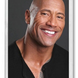 May include: A close-up portrait of a man with a shaved head, smiling with his teeth showing. He is wearing a black shirt with a button at the neck.