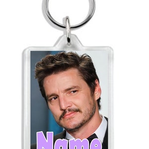 May include: A clear acrylic keychain featuring a photo of a man with brown hair and a moustache. The text "Name" is printed in purple letters at the bottom of the photo.