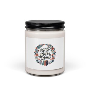 Peut inclure: Un pot à bougie en verre transparent avec un couvercle en métal noir, rempli de cire blanc cassé. L'étiquette avant présente une couronne florale entourant le texte "cool girls read" en écriture cursive, avec trois petits livres colorés illustrés en bas.