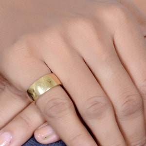 May include: A gold band ring worn on a person's finger.