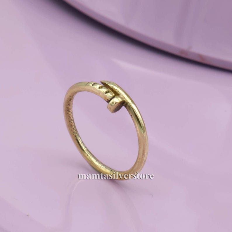 May include: A gold-toned ring with a nail design. The nail is wrapped around the band of the ring.