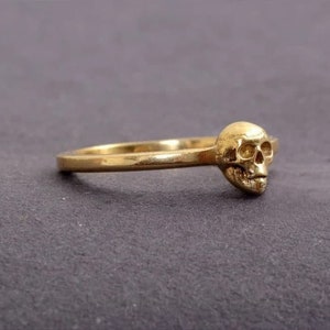 May include: A gold ring featuring a skull design. The skull is detailed and has a three-dimensional appearance.