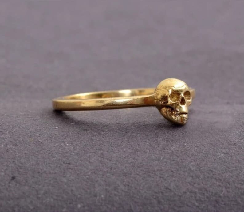 May include: A gold ring featuring a skull design. The skull is detailed and has a three-dimensional appearance.
