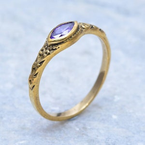 Peut inclure: Une bague en or avec une pierre précieuse de forme marquise violette sertie dans un motif floral.