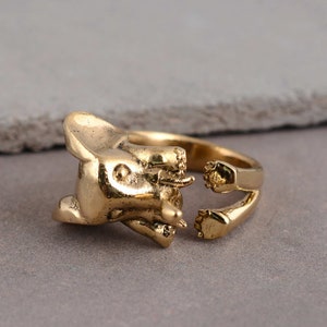 Puede incluir: Un anillo de tono dorado con un diseño de elefante detallado. El anillo está abierto por un lado, lo que permite ajustarlo a diferentes tamaños de dedos.