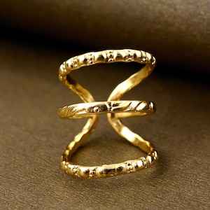 May include: Gold ring with three bands, each with a different texture. The top band has small dots, the middle band has a wavy pattern, and the bottom band has small dots.