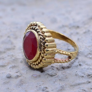 May include: A gold ring with a red gemstone set in a decorative, ornate setting.