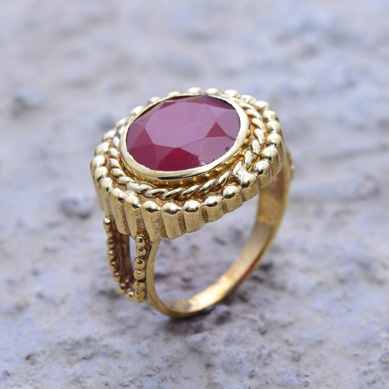 May include: A gold ring featuring a large, red gemstone set in an ornate, decorative setting.