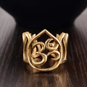 May include: A gold-colored ring with an intricate design featuring the Om symbol within a lotus flower shape.