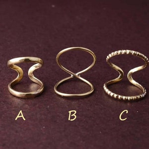 以下が含まれることがあります： 異なるデザインの3つの金色リング。'A'とラベル付けされたリングは、シンプルで滑らかなダブルループデザイン。'B'とラベル付けされたリングは、中央にねじれたダブルループデザイン。'C'とラベル付けされたリングは、外側に小さなビーズが付いたダブルループデザインです。