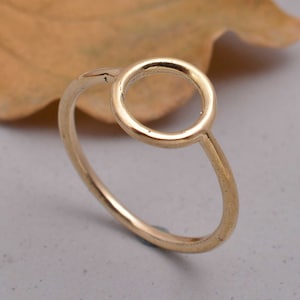 May include: A simple gold ring with a large circle design. The ring is made of a thin band of metal and the circle is open.