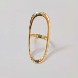 Könnte beinhalten: Ein goldfarbener ovaler Ring mit einem großen, offenen Raum in der Mitte. Der Ring ist aus glattem Metall gefertigt und hat ein schlichtes, modernes Design.