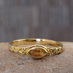 Op de afbeelding: Een gouden ring met een marquise-vormige topaas-edelsteen gezet in een delicate, sierlijke band.