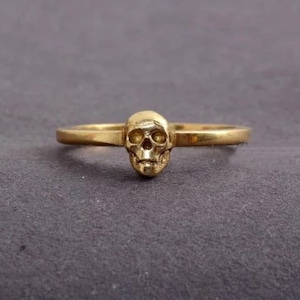 May include: A gold skull ring with a simple band.