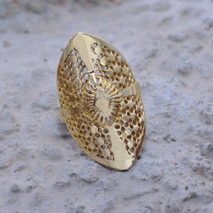 Könnte beinhalten: Ein goldfarbener Ring mit ovalem Design. Der Ring besteht aus einem filigranen, komplizierten Muster aus kleinen Kreisen und Quadraten.