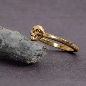 May include: A gold skull ring featuring a detailed skull design. The ring is crafted from smooth, shiny metal and has a simple band.