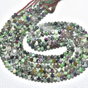 May include: Strands of faceted gemstone beads in shades of green, gray, and burgundy. The beads are strung together, forming a circular pattern. The beads are small, and the overall effect is delicate and intricate. The beads are likely used for jewelry making.