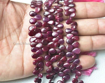 May include: A strand of deep red ruby gemstone beads in a teardrop shape. The beads are strung on a clear thread and are approximately 10mm in size.