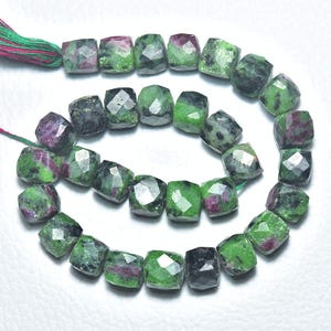 Puede incluir: Un hilo de cuentas de piedras preciosas facetadas. Las cuentas son de forma cuadrada, con una mezcla de colores verde, gris oscuro y rojo-púrpura. El hilo que sostiene las cuentas tiene una borla verde y roja.