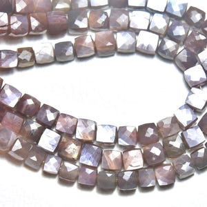 May include: Strands of faceted square beads in shades of gray, lavender, and brown. The beads are strung together, creating a necklace or bracelet. The beads have a polished, reflective surface.