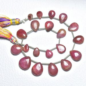 May include: Strands of polished, teardrop-shaped gemstones in varying shades of red and pink. The beads are strung on a silver wire, with a colourful tassel at the end. The gemstones are approximately 1 cm in length.