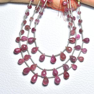 May include: Strands of pink gemstone beads. The beads are a mix of round and teardrop shapes, strung on silver-colored wire. The gemstones have a faceted surface, catching the light. The beads are arranged in multiple layers.