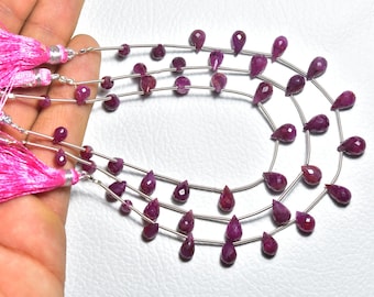 May include: A strand of ruby gemstone beads in a teardrop shape. The beads are strung on silver wire and are approximately 10mm in size. The beads are a deep red color and have a high polish.