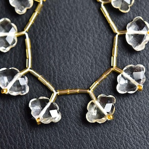 Peut inclure: Un collier composé de perles transparentes à facettes en forme de trèfle, alternées avec de petites perles intercalaires cylindriques de couleur or métallique. Les perles transparentes présentent une surface à facettes réfléchissant la lumière.