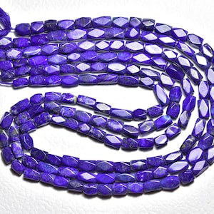 Puede incluir: Un collar de cuentas facetadas de lapislázuli azul profundo. Las cuentas son oblongas con un corte geométrico y están ensartadas con un hilo azul a juego. Las cuentas están dispuestas en un patrón en espiral, con una borla de hilo azul en la parte superior.