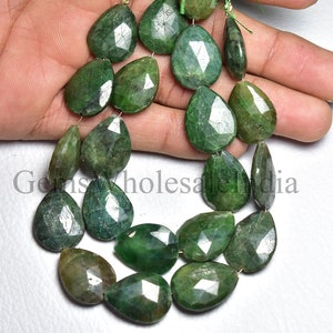 May include: A strand of faceted, pear-shaped emerald gemstones. The gems are a deep green colour with visible facets, strung together on a thin thread. The image is well-lit, showcasing the clarity and colour of the stones. The overall theme is jewellery and gemstones.