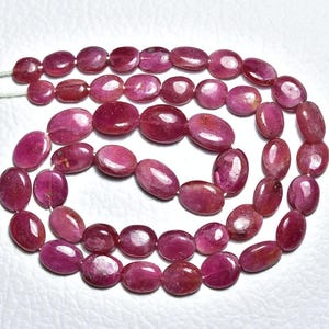以下が含まれることがあります： 楕円形に研磨されたルビービーズの連なり。ビーズは深く豊かな赤色で、白い糸で繋がれています。宝石は滑らかで自然な有機的な形をしており、ジュエリー作りに最適です。