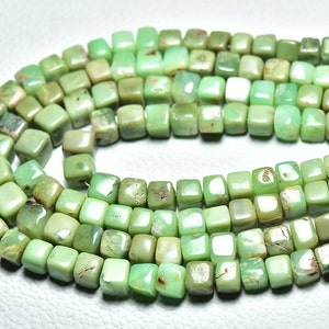 Puede incluir: Una hebra de cuentas de piedras preciosas verdes, cada cuenta tiene forma cuadrada. Las cuentas están enhebradas en un alambre y están listas para ser utilizadas para la elaboración de joyas.