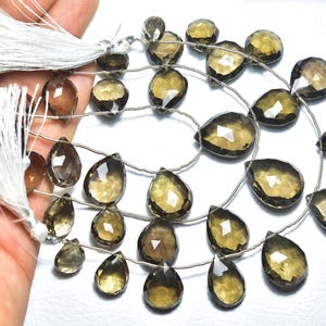 May include: A strand of brown gemstone beads with a faceted teardrop shape. The beads are strung on a silver wire and have a natural, earthy look.